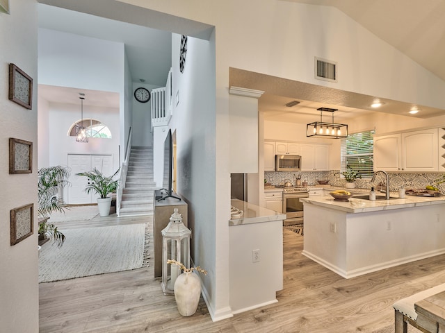 kitchen with appliances with stainless steel finishes, light hardwood / wood-style flooring, white cabinets, and tasteful backsplash