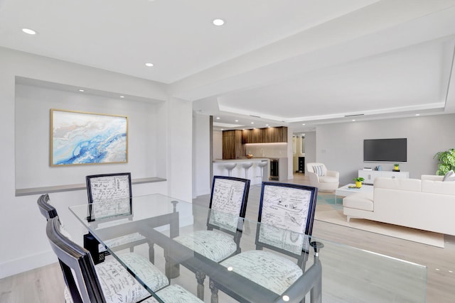 dining space with a tray ceiling and light wood-type flooring