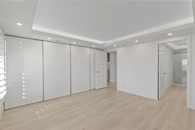 unfurnished bedroom with light hardwood / wood-style flooring and a tray ceiling