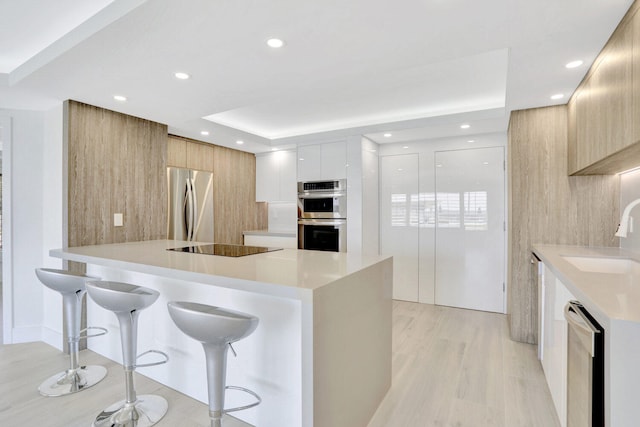 kitchen featuring white cabinets, appliances with stainless steel finishes, a kitchen breakfast bar, light wood-type flooring, and sink