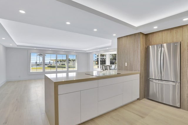 kitchen with stainless steel fridge, white cabinetry, light hardwood / wood-style flooring, and a raised ceiling