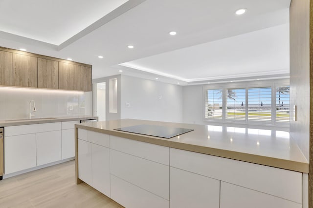 kitchen featuring sink, light wood-type flooring, a raised ceiling, black electric cooktop, and white cabinets