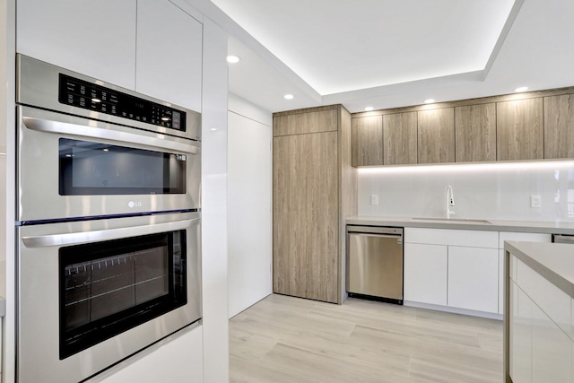 kitchen with white cabinets, appliances with stainless steel finishes, a tray ceiling, light hardwood / wood-style flooring, and sink