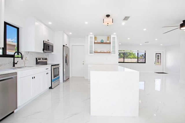 kitchen with a kitchen island, backsplash, sink, white cabinets, and appliances with stainless steel finishes