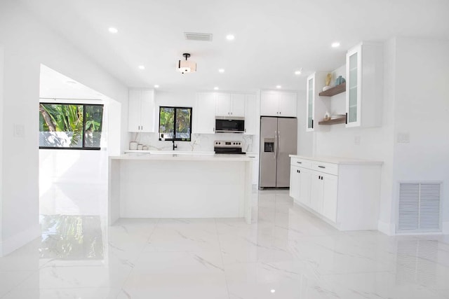 kitchen featuring tasteful backsplash, kitchen peninsula, stainless steel appliances, decorative light fixtures, and white cabinets