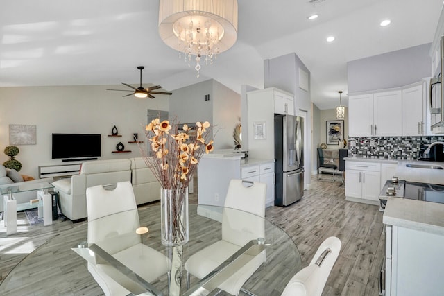 dining room with light wood-type flooring, ceiling fan with notable chandelier, sink, and high vaulted ceiling