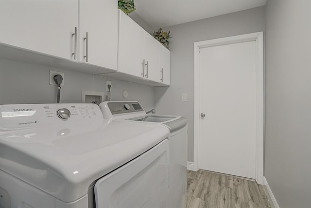 clothes washing area with cabinets, washing machine and dryer, and light wood-type flooring