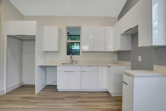 kitchen with white cabinets, light hardwood / wood-style floors, sink, and vaulted ceiling