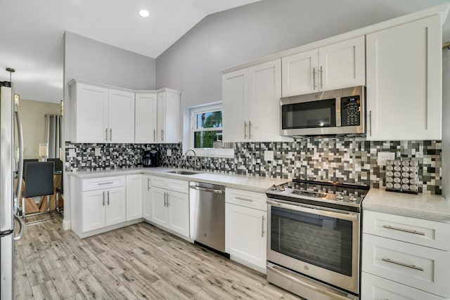 kitchen featuring lofted ceiling, sink, white cabinetry, light wood-type flooring, and appliances with stainless steel finishes