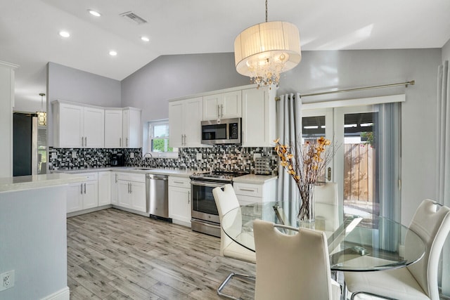 kitchen with white cabinetry, stainless steel appliances, hanging light fixtures, and light hardwood / wood-style flooring