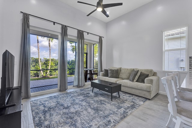 living room featuring ceiling fan, a high ceiling, and light wood-type flooring