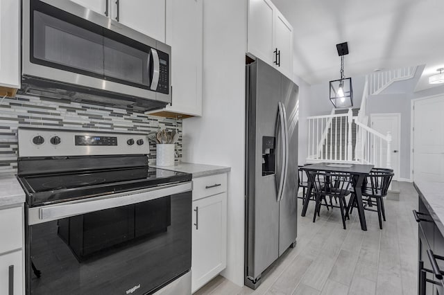 kitchen with backsplash, appliances with stainless steel finishes, white cabinetry, and pendant lighting