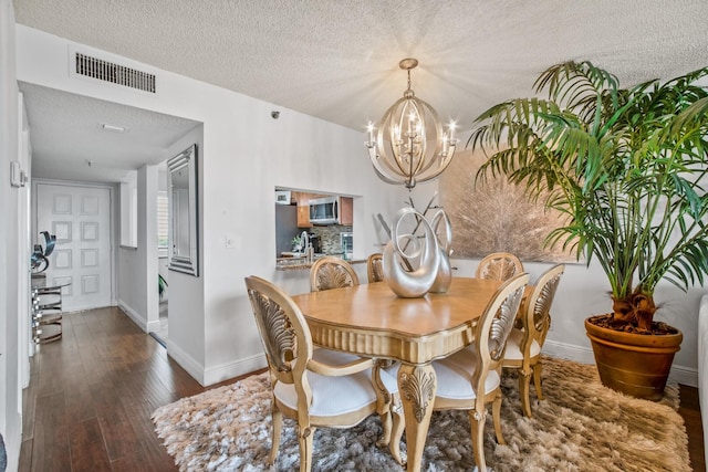 dining space featuring dark wood-type flooring, a textured ceiling, and an inviting chandelier