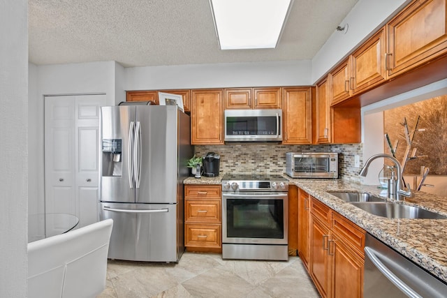 kitchen featuring light stone counters, stainless steel appliances, a textured ceiling, and sink