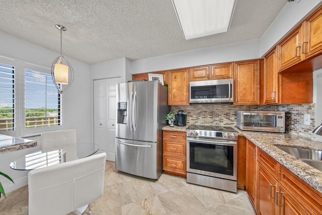 kitchen featuring stainless steel appliances, light stone countertops, pendant lighting, a textured ceiling, and tasteful backsplash