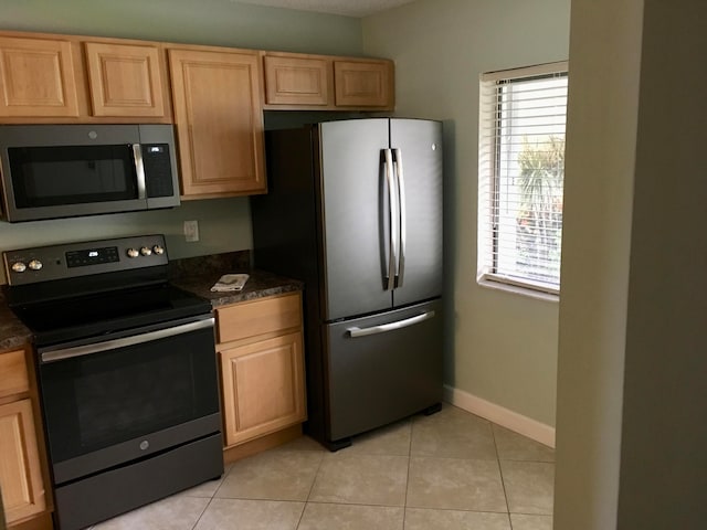 kitchen featuring light tile patterned flooring, dark stone countertops, light brown cabinetry, and appliances with stainless steel finishes