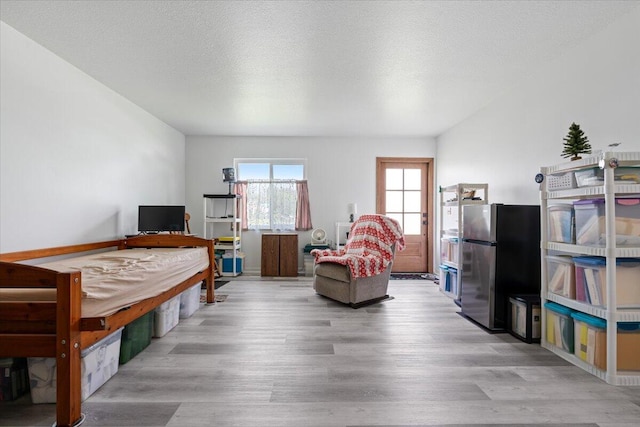 bedroom featuring stainless steel fridge, a textured ceiling, and light wood-type flooring