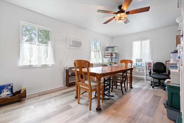 dining room with light hardwood / wood-style floors, a wall unit AC, a healthy amount of sunlight, and ceiling fan