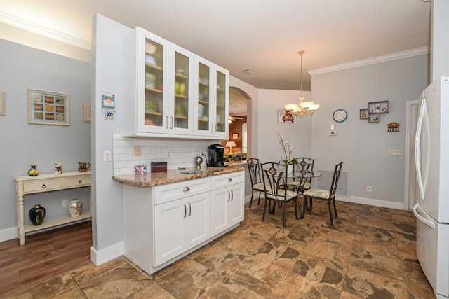 kitchen with light stone counters, hanging light fixtures, tasteful backsplash, white fridge, and white cabinetry