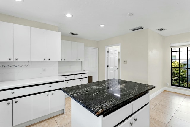 kitchen with white cabinets, dark stone countertops, a kitchen island, and light tile patterned floors