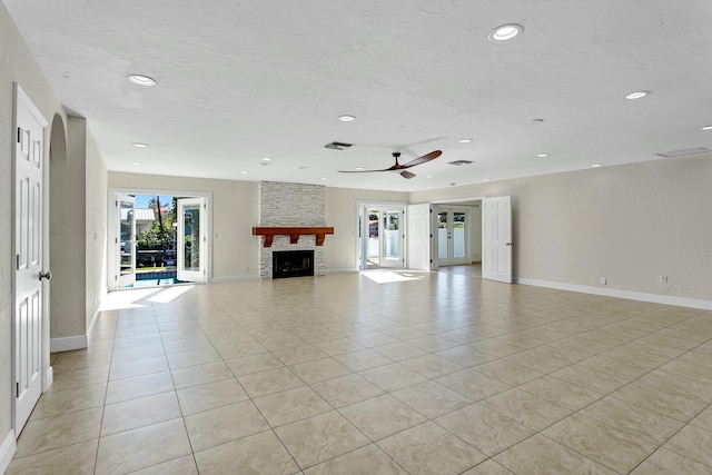 unfurnished living room featuring ceiling fan, light tile patterned flooring, and a stone fireplace