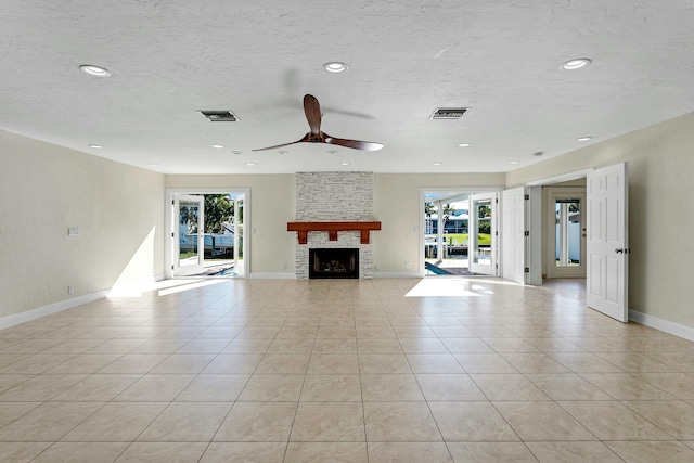 unfurnished living room with a stone fireplace, ceiling fan, light tile patterned floors, and a healthy amount of sunlight