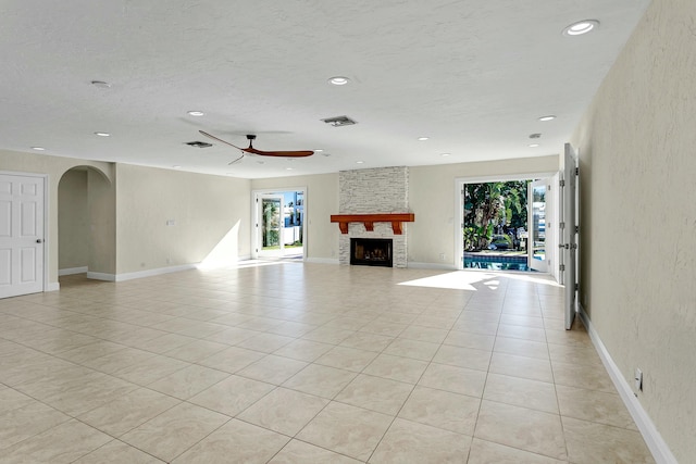 unfurnished living room featuring a stone fireplace, a wealth of natural light, ceiling fan, and light tile patterned flooring