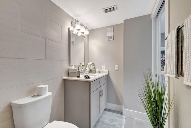 bathroom with tile walls, vanity, toilet, and concrete floors