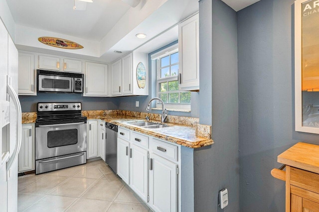 kitchen with stainless steel appliances, sink, light tile patterned floors, white cabinets, and light stone counters