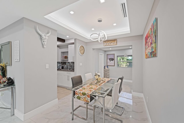 dining space with a tray ceiling, sink, and a chandelier