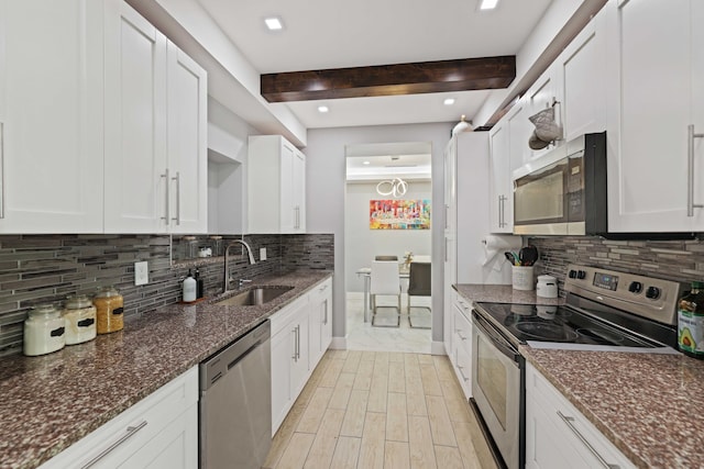 kitchen with beam ceiling, sink, stainless steel appliances, dark stone countertops, and white cabinets