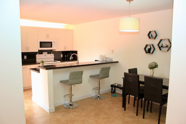 kitchen with kitchen peninsula, white cabinetry, a kitchen bar, decorative light fixtures, and white appliances