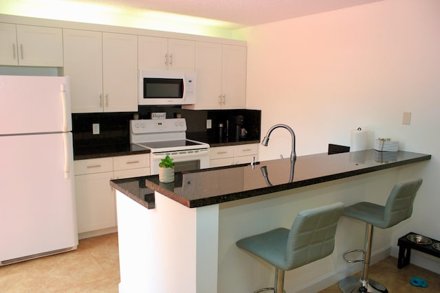 kitchen featuring white appliances, white cabinetry, a breakfast bar area, and decorative backsplash