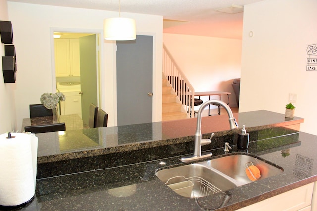 kitchen with washer / dryer, sink, decorative light fixtures, white cabinets, and dark stone countertops