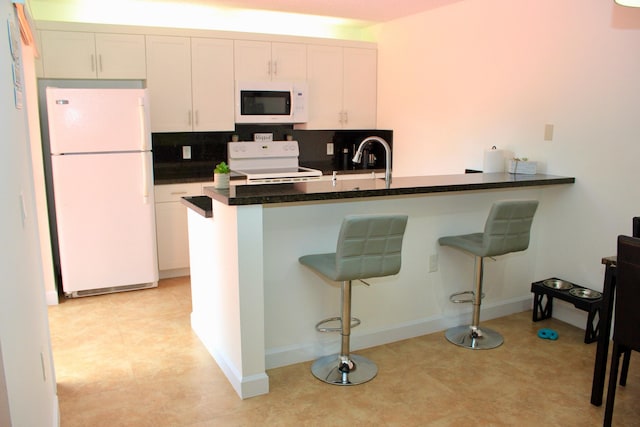 kitchen featuring a kitchen breakfast bar, kitchen peninsula, backsplash, white cabinets, and white appliances