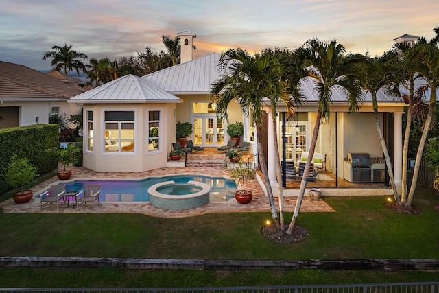 back house at dusk with a yard, french doors, a patio, and a pool with hot tub