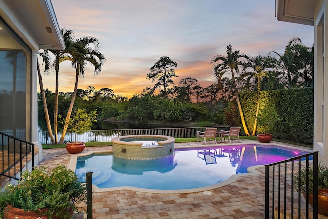 pool at dusk featuring an in ground hot tub, a patio, and a water view