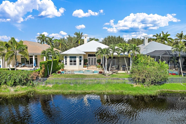 back of house with a patio area, an in ground hot tub, glass enclosure, and a water view