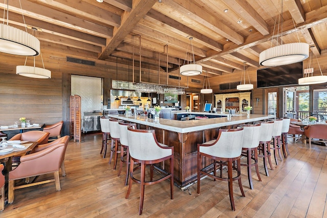 kitchen with a large island, wood walls, hardwood / wood-style flooring, pendant lighting, and beam ceiling