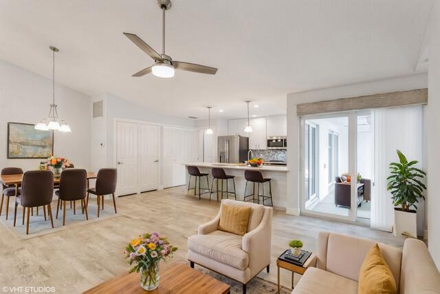 living room featuring ceiling fan with notable chandelier, vaulted ceiling, and light hardwood / wood-style flooring