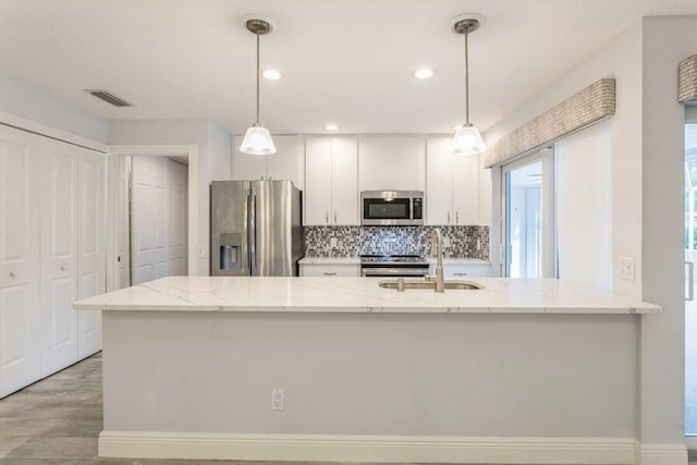 kitchen with light stone countertops, decorative light fixtures, stainless steel appliances, white cabinets, and sink