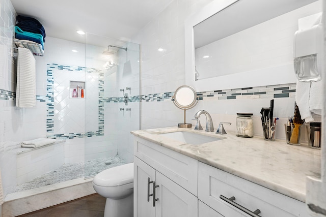 bathroom featuring decorative backsplash, a tile shower, vanity, tile walls, and toilet