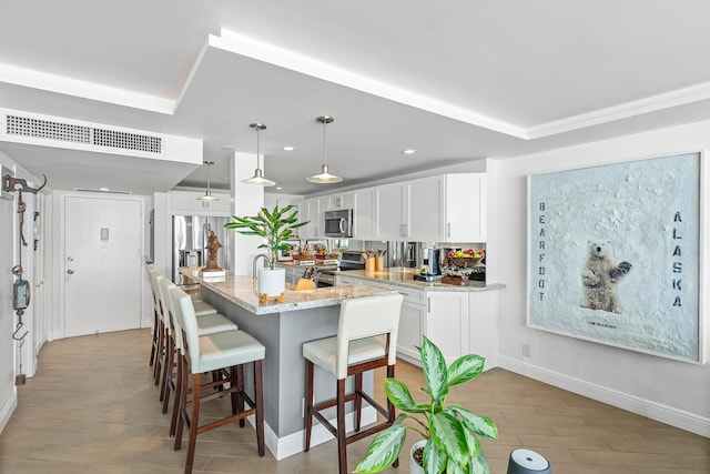 kitchen with white cabinets, hanging light fixtures, light stone countertops, appliances with stainless steel finishes, and wood-type flooring