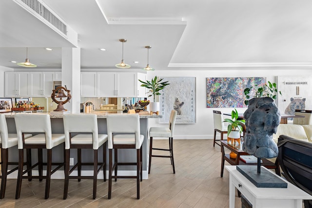 kitchen featuring light stone countertops, a tray ceiling, decorative light fixtures, white cabinets, and a breakfast bar area