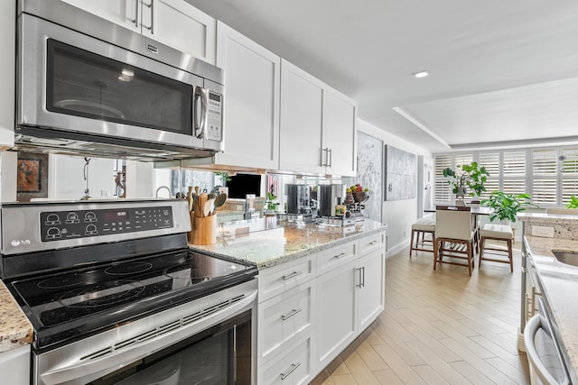 kitchen featuring stainless steel appliances, white cabinetry, light hardwood / wood-style floors, and light stone counters