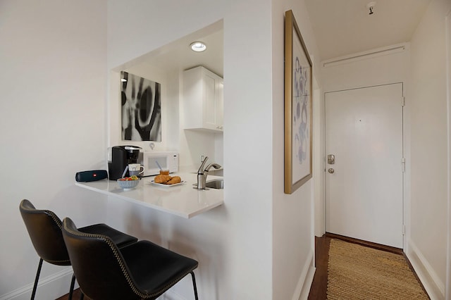 kitchen with wood-type flooring, kitchen peninsula, a breakfast bar area, sink, and white cabinetry