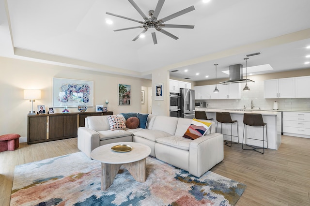 living room with sink, a skylight, light wood-type flooring, and ceiling fan