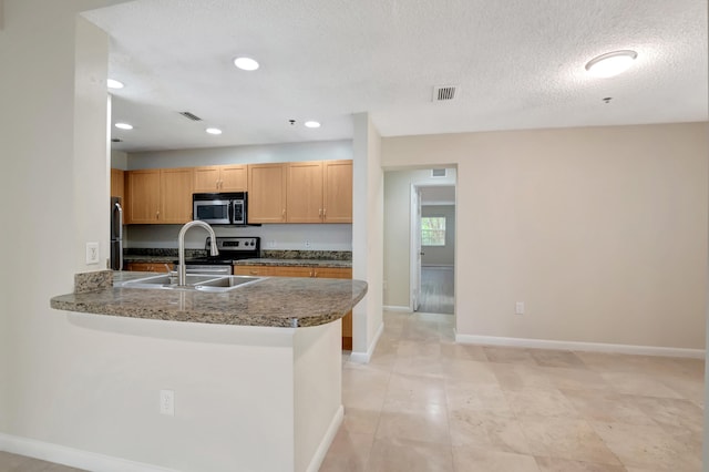 kitchen with appliances with stainless steel finishes, sink, a textured ceiling, kitchen peninsula, and dark stone counters