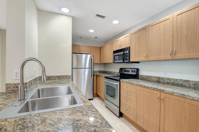 kitchen with light stone counters, stainless steel appliances, sink, and light brown cabinetry