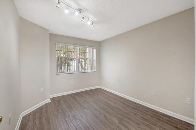 empty room with a textured ceiling, track lighting, and dark wood-type flooring